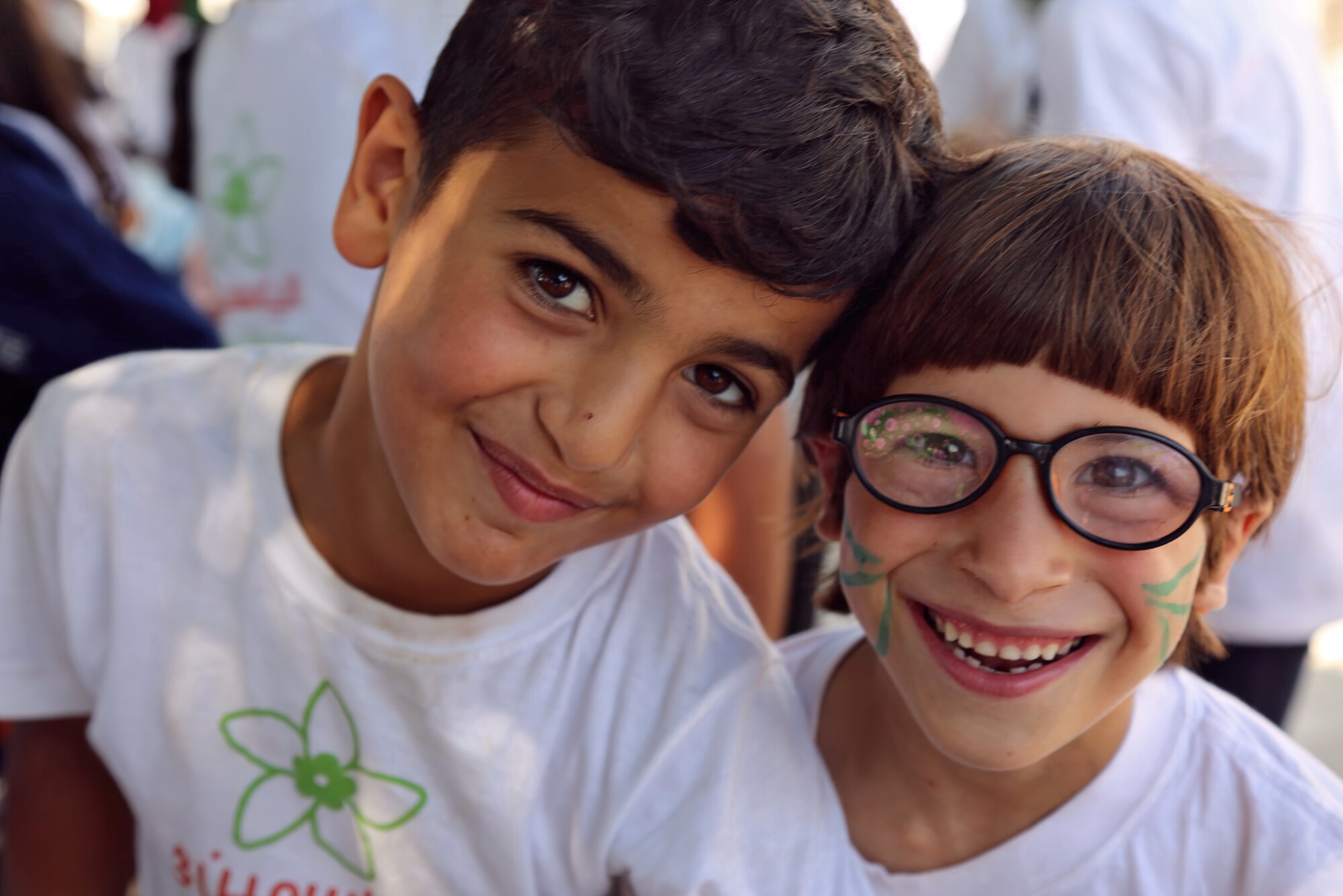 Two kits lean their heads together. One kid has face paint.